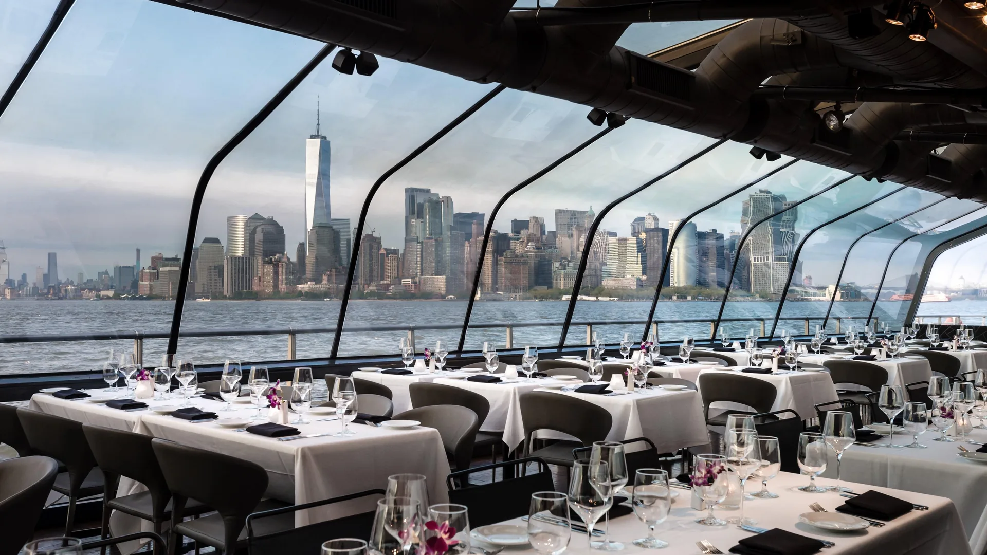 Laid tables under the glass roof of City Cruises' luxury dining boat with the downtown skyline outside, from the luxury cruise listing